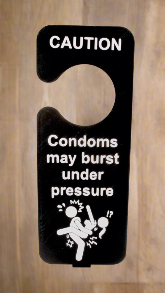 Door hanger with 'CAUTION: Condoms may burst under pressure' text and graphic on a wooden background