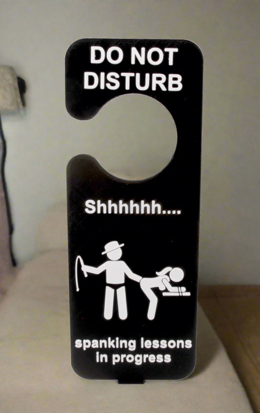 Door hanger with 'Do Not Disturb' and 'Spanking lessons in progress' text on a white background